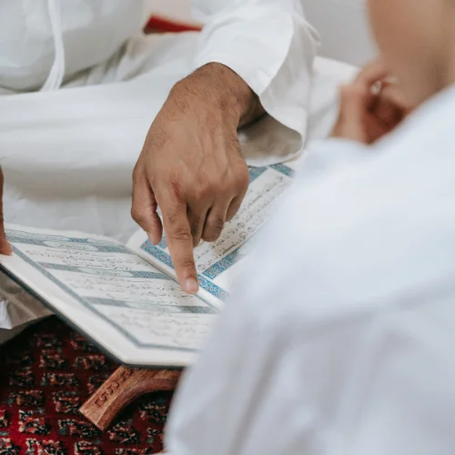 A close-up shot of two individuals in white attire studying the Quran.